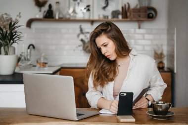 Genç bayan evde dizüstü bilgisayarın önünde notlar alıyor. Evden çalışıyorum. Eğitim ve iletişim kavramı.