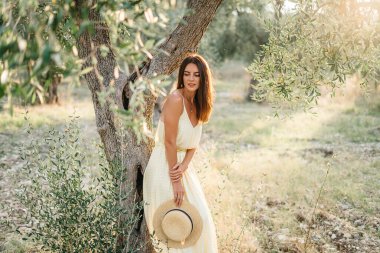 Güzel gün ışığında güzel esmer bir kadının narin portresi. Sarı keten elbiseli kadın zeytin ağacı bahçesinde. Doğal güzellik. İtalya 'ya seyahat, yaz tatili.