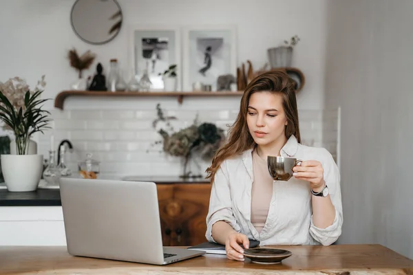 Mulher sorridente trabalhando com laptop enquanto toma café da manhã em casa — Fotografia de Stock