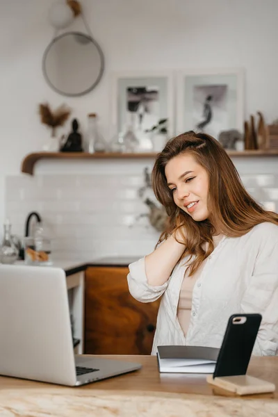 Gelukkig aantrekkelijk jong vrouw zitten in haar keuken aan de toonbank met een laptop glimlachen op de camera — Stockfoto