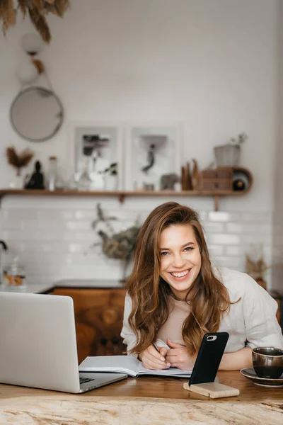 Gelukkig aantrekkelijk jong vrouw zitten in haar keuken aan de toonbank met een laptop glimlachen op de camera — Stockfoto