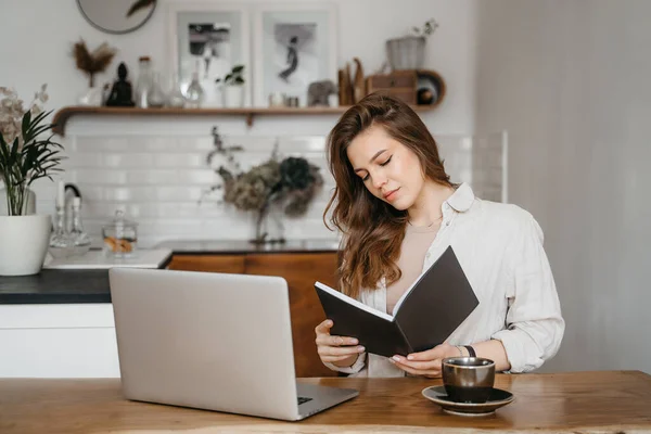 Mujer joven toma notas delante de la computadora portátil en casa. Trabajando desde casa. Concepto de educación y comunicación. — Foto de Stock