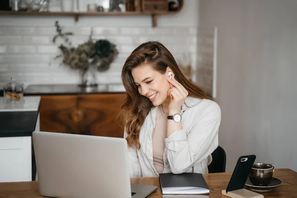 Feliz joven atractiva sentada en su cocina en el mostrador con un portátil sonriendo a la cámara — Foto de Stock