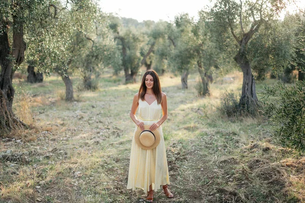 Delikatny portret pięknej brunetki w pięknym słońcu. Kobieta w żółtej letniej bieliźnie sukienka w ogrodzie drzewa oliwnego. Podróż do Włoch, letnie wakacje — Zdjęcie stockowe