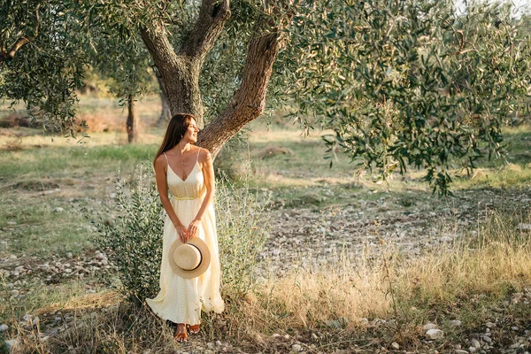Delikatny portret pięknej brunetki w pięknym słońcu. Kobieta w żółtej letniej bieliźnie sukienka w ogrodzie drzewa oliwnego. Podróż do Włoch, letnie wakacje — Zdjęcie stockowe