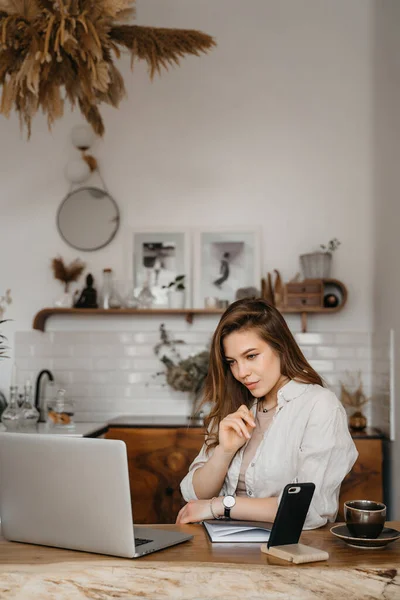 Feliz joven atractiva sentada en su cocina en el mostrador con un portátil sonriendo a la cámara — Foto de Stock