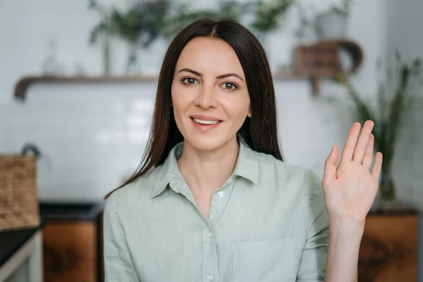 young woman waving hand waving hand into camera with a smile. Video call, virtual conference