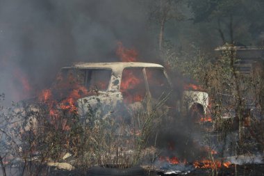 Ateşle kaplı bir arazide yanan araba.
