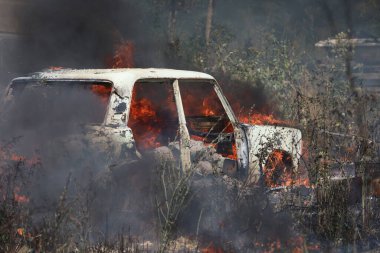 Ateşle kaplı bir arazide yanan araba.
