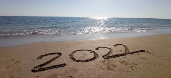 Happy New Year 2022, lettering on the beach with wave and clear blue sea. Numbers 2022 year on the sea shore, message handwritten in the golden sand on beautiful beach background. New Years concept.