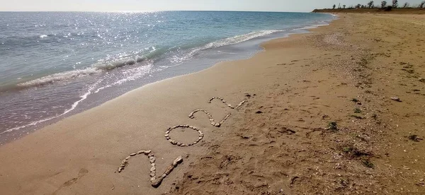 Happy New Year 2022, lettering on the beach with wave and clear blue sea. Numbers 2022 year on the sea shore, message handwritten in the golden sand on beautiful beach background. New Years concept.