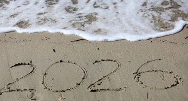 New Year 2026, lettering on the beach with wave and clear blue sea. Numbers 2026 year on the sea shore, message handwritten in the golden sand on beautiful beach background. New Years concept.