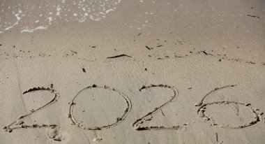 New Year 2026, lettering on the beach with wave and clear blue sea. Numbers 2026 year on the sea shore, message handwritten in the golden sand on beautiful beach background. New Years concept.