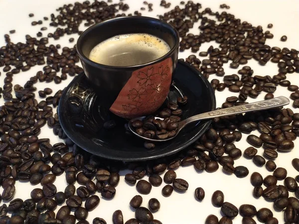 Etrafına dağılmış kahve çekirdekleri serpiştirilmiş, beyaz arka planda yeni demlenmiş kahve fincanına yakından bakın.