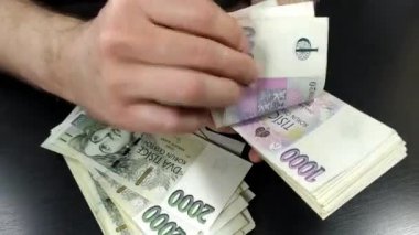 Bin kron Çek banknotunu elinde tutan ve onları sayan bir erkeğin görüntüsü, arka planda iki bin kron banknot yığını