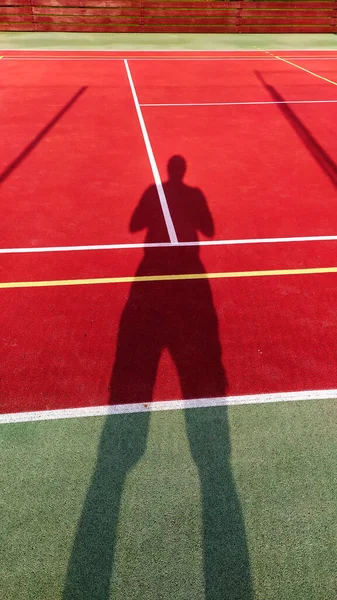 Tenis kortunda ayakta duran bir adamın gölgesi tenis kortunda oynayan bir tenisçinin gölgesi.
