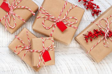 Beyaz ahşap arka planda noel hediyelerinin en üst görüntüsü. El işi kağıtları, çizgili ip ve kutsal meyvelerle süslenmiş hediye kutuları. Yeni yıl düzlüğü. 