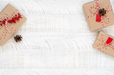 Noel hediyeleri el sanatları kağıdına sarılıp beyaz ahşap zemin üzerine kutsal böğürtlen ve çam kozalaklarıyla süslenmiş. Üst Manzara. Hediye kutuları.