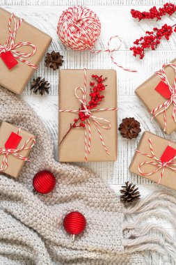 El yapımı hediyelerin en üst görüntüsü. Çam kozalaklarıyla bembeyaz bir Noel yatağı, el sanatları kağıdına sarılı hediyeler ve çizgili fırıncının sicimi ve ahşap arka planda kutsal meyvelerle süslenmiş..