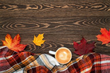 Sıcacık ve sıcak sonbahar dairesi fotokopi alanı ile yatıyordu. Hygge konsepti. Kahvenin üst görüntüsü, ekose eşarp, kırmızı, turuncu ve sarı akçaağaç yaprakları ahşap arka planda.. 
