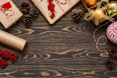 Süslü hediyeleri ve kahverengi ahşap arka planda süsleri olan bir Noel dairesi. Yeni yıl hediyeleri, kutuda mücevherler, çam kozalakları, sicim teli, el işi kağıt ve kutsal çilek. Boşluğu kopyala.