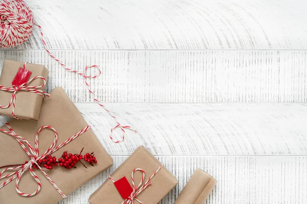 Christmas gifts on white wooden background with copy space. Top view of twine, craft paper and new year presents.