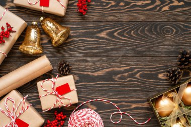 Noel hediyelerinin en üst görüntüsü ve ahşap arka planda çeşitli süsler. Yeni yıl hediyeleri, mücevherler kutuda, altın çanlar, kutsal böğürtlenler, sicim telleri ve çam kozalaklarıyla yatıyordu. Boşluğu kopyala.