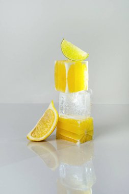 Birbirinin üzerine buz küpü ve limon dilimleri konmuş taze limon dilimleri. Soğuk sulu limonata konsepti. Gri arka planda yaz içeceği
