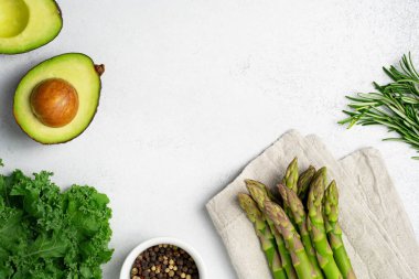 Yeşil sebzeler ve gri arka planda bitkiler. Peçete, avokado, lahana, biberiye ve biber karışımı taze çiğ kuşkonmaz..