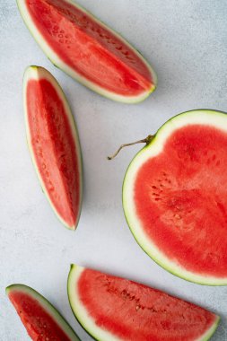 Kırmızı karpuz parçaları ve yarısı gri arkaplanda. Taze olgun sulu meyve dilimleri. Vitaminli ve antioksidanlı paleo diyeti için sağlıklı yaz atıştırmalıkları. Detoks konsepti. Üst manzara, düz uzanma