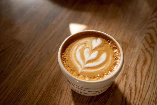 Kopi dengan latar belakang kayu. Secangkir cappuccino dengan busa susu di atas meja coklat di kafe. Putih datar dengan seni latte yang indah — Stok Foto
