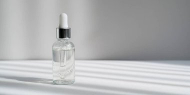 Şeffaf cam damlası şişesinde sert gölgeli yüz serumu. Gri arka plan web afişinde pipetli nemlendirici kozmetik ürün. Kolajen ve peptitlerle cilt bakımı jeli