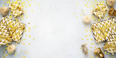Hediye kutuları ve altın süslemeleri olan Noel afişi. Kağıt süslemeler, parlak çanlar, şekerler, yıldız konfetileri, gri arka planda hediyeler. Yeni yıl kompozisyonu. Düz konum, Üst görünüm, kopyalama alanı