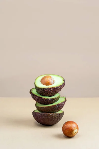 Fresh ripe avocado cut in half stacked on top of each other and avocado seed on beige background. Balanced food concept. Healthy diet composition. Vegetable with vitamins and antioxidants. Copy space