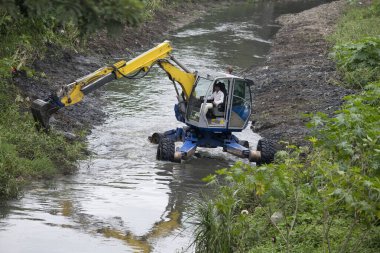 Nehir tarama ve nehir kıyılarını temizlemek için özel lastikleri olan kazıcı. Konumu: Nashik, Maharashtra, Hindistan. Tarih - 14 Ağustos 2021