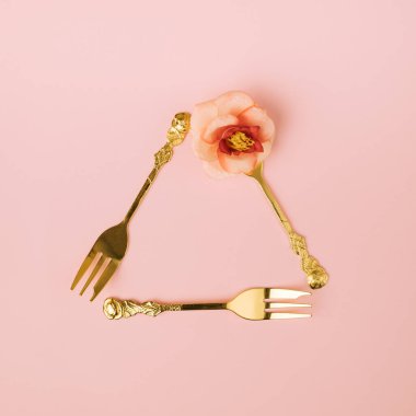 Minimum yaratıcı altın çatal kavramı, çiçekli üçgen sembolü, pastel pembe arka planda oluşturur. Kutlama fikri