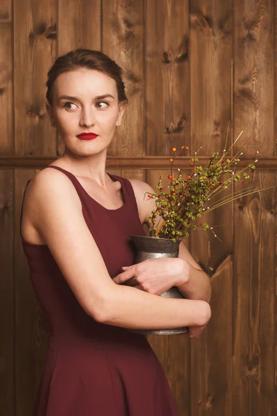 Porträtt av en vacker flicka i en vinröd klänning på en bakgrund av en trävägg — Stockfoto