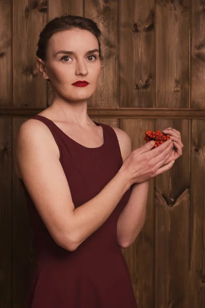 Girl holding a rowan on a background of a wooden wall — Stock Photo, Image