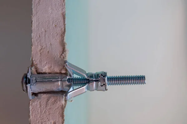 Metal Molly sabitleyici, önceden delinmiş bir delikten nem geçirmez alçıpan tabakasına sabitlenmiş, bölünmüş görüntü. Yaprak kurulum alanında kesilir, alçı taşı lifini ve bağlantı detaylarını gösterir.