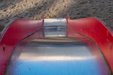 Pürüzsüz, pürüzsüz metal tabanlı ve tahta kırmızı tırabzanlar, oyun parkında ayak izleriyle kaplı kumla kaplı olarak, dik bir şekilde yüzeye iniyor. Kavram: Kazanılan pozisyonlardan düşme olasılığı