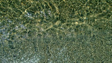 Küçük çakıl taşlarıyla sarı kumlu zeminin üzerindeki gök mavisi deniz suyu parlak yansımaları ve yıldızlarla parıldıyor ve ışık çizgileriyle çekici bir desen oluşturuyor. Tasarım için doğal, organik arkaplan.