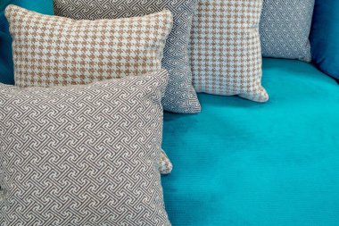 Orta boy kabarık yastıklar gri, bej ve kahverengi desenli döşemeli koltuğun açık mavi kumaş döşemesinde birbiri ardına yatıyorlar. Soyut iç tasarım arka planı.