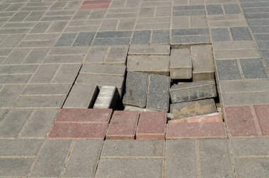 Gri ve pembe bloklarla döşenmiş kaldırım geçidini kırın, batık toprağı ve çukura düşen birkaç kiremit görebilirsiniz. Kavram: Yetersiz yürütülen yol çizgisi çalışmaları ve hava durumu.
