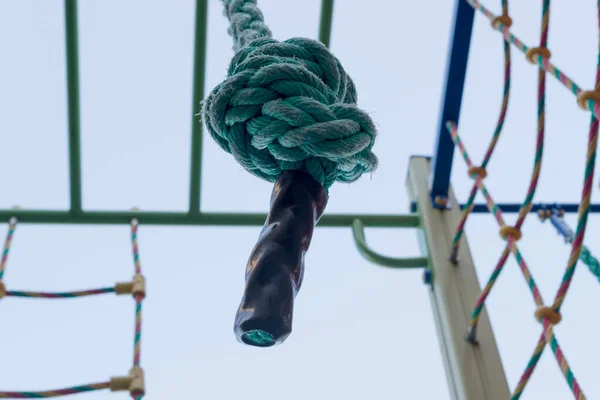 ラック 色のロープはしごや遊び場の登山ネットを背景に水平バーのクロスバーからぶら下がっ結び目のターコイズスポーツロープの終わり コンセプト 目標達成への挑戦 — ストック写真