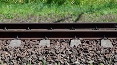 Demir rayların ve beton pusuculardan oluşan demiryolu yüzeyi granit taşların üzerine serilmiş, rayların arkasında yeşil çimenler yetişiyor. Bazı arabaların yüksek hızda geçtiği tekerlekleri ve trenin alt kısmını görebilirsiniz..
