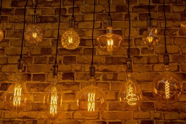 Kahverengi tuğla duvarın arka planında parlak iplikler bulunan saydam parlak lambalardan oluşan sıralar. Konsept: ev eşyalarının gece ışıklandırması teması