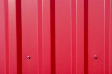 Corrugated galvanize demir tipine ait kırmızı metal bir profil parçası tabanına baskı makinası ve altıgen başlıklı çatı vidalarıyla tutturulmuş. Çitleri ve çatıları örtmek için kullanılır..