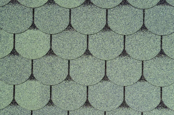 Roof grainy bituminous coating for the rooftop with a pattern in the form of scaly tiles in bluish green color with a black outline. Industrial construction background for design.