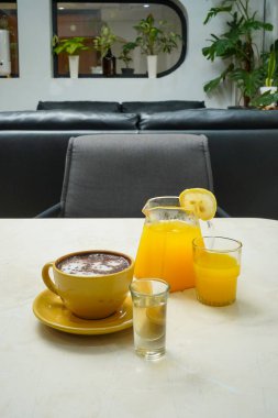 Sarı kahve fincanı, bir bardak portakal suyu ve bir bardak likör.