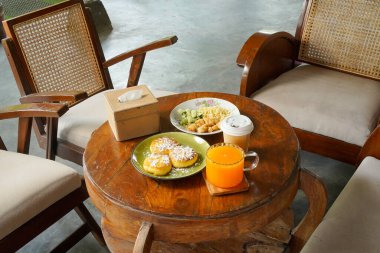 İçinde bir tabak yemek ve bir fincan portakal suyu olan bir masa. Masanın etrafında sandalyeler var.